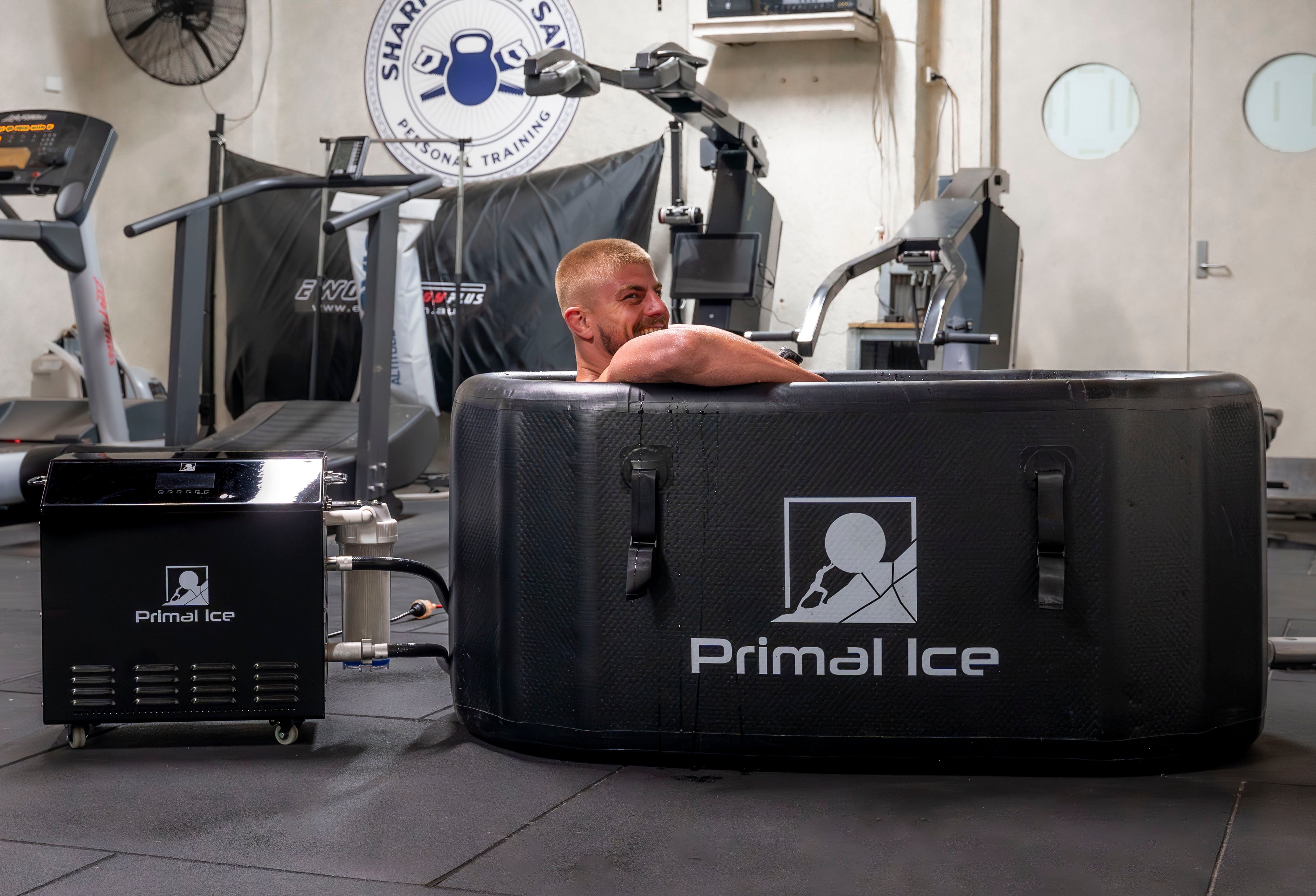 man inside primal ice bath tub connected to commercial ice bath chiller inside a gym